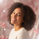 A smiling young woman, mid-shot, with a happy expression against a soft pink and white background.